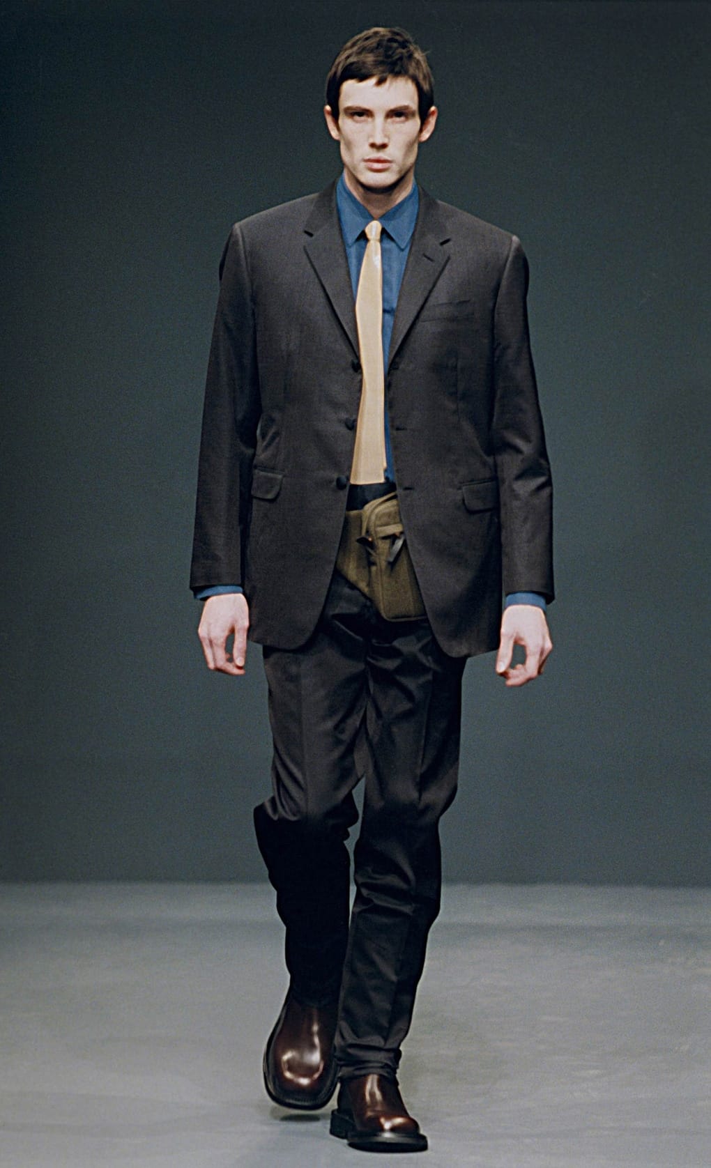 Prada Fall/Winter 1999 menswear runway look 71: black suit with blue shirt, tan tie, and tall boots.