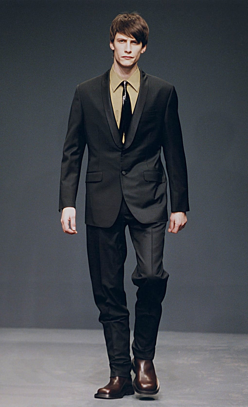 Prada Fall/Winter 1999 menswear runway look 74: black suit with pale shirt, black tie, and dark cropped trousers.