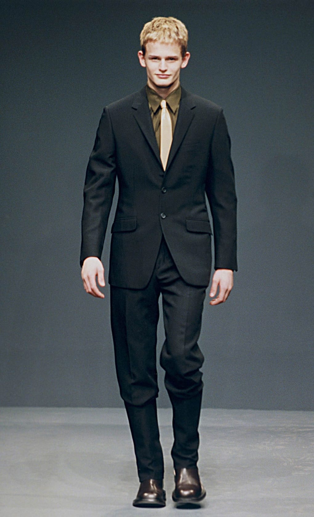 Prada Fall/Winter 1999 menswear runway look 76: black suit with olive shirt and slim black trousers.