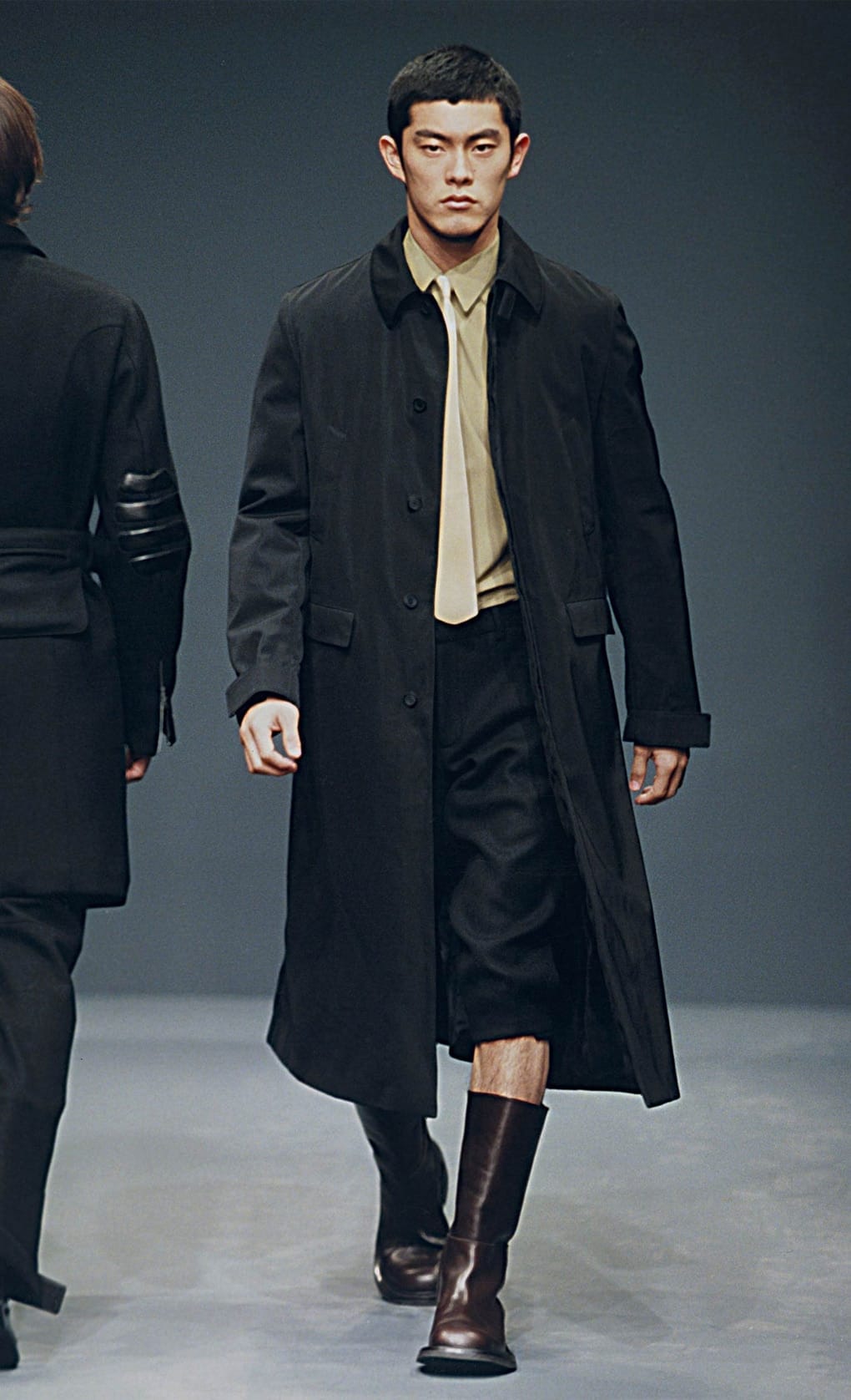 Prada Fall/Winter 1999 menswear runway look 78: long black coat over an olive shirt and cropped trousers.