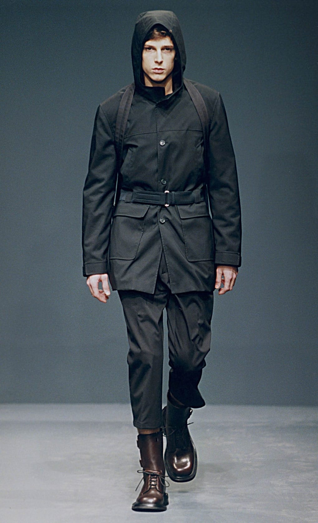 Prada Fall/Winter 1999 menswear runway look 79: black hooded belted jacket with cropped trousers and boots.