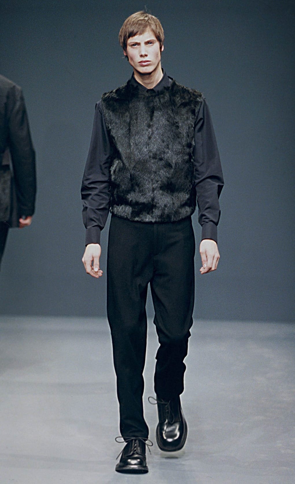 Prada Fall/Winter 1999 menswear runway look 80: black fur-front top with dark trousers and black shoes.