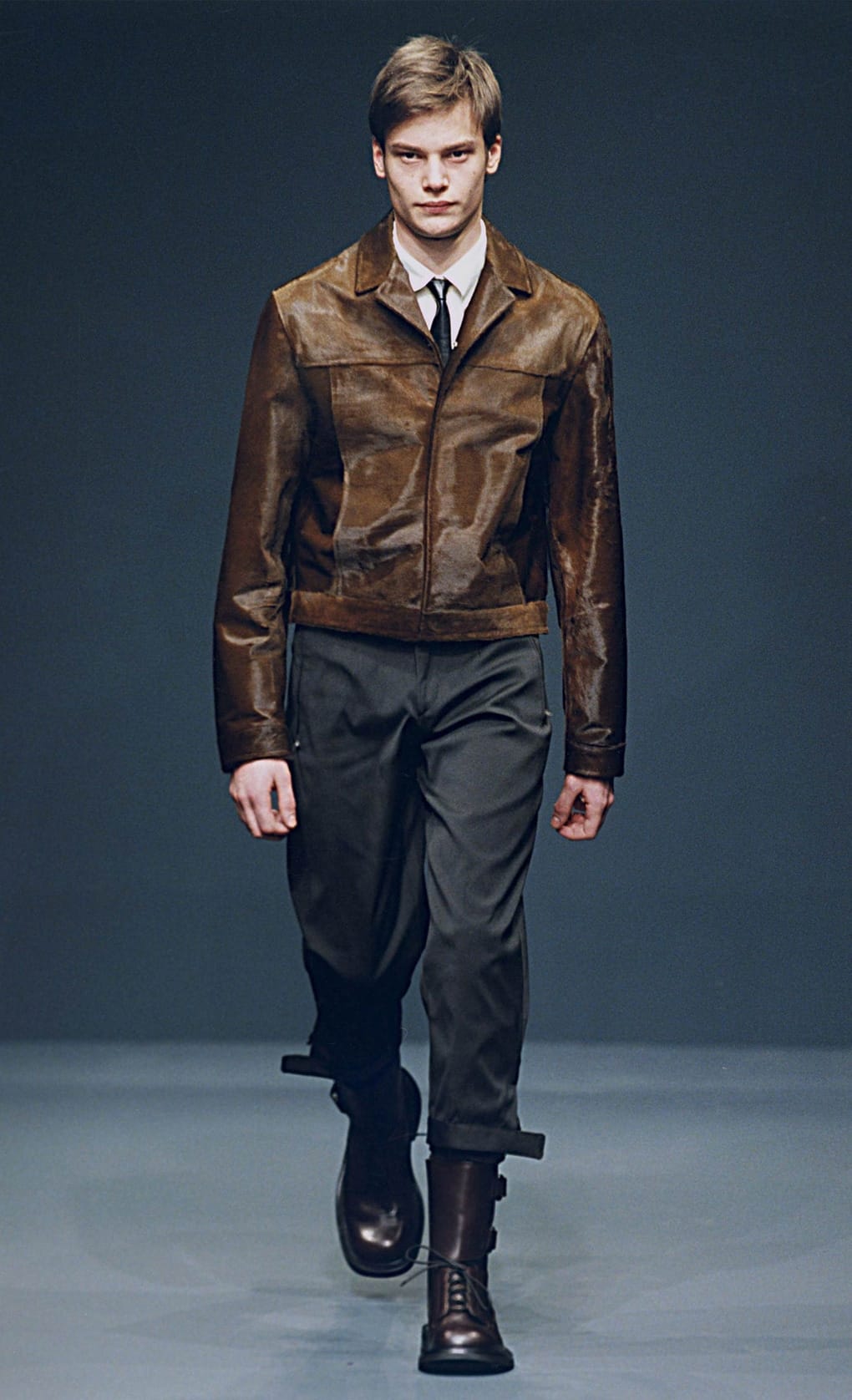 Prada Fall/Winter 1999 menswear runway look 9: brown leather jacket with dark trousers and lace-up boots.
