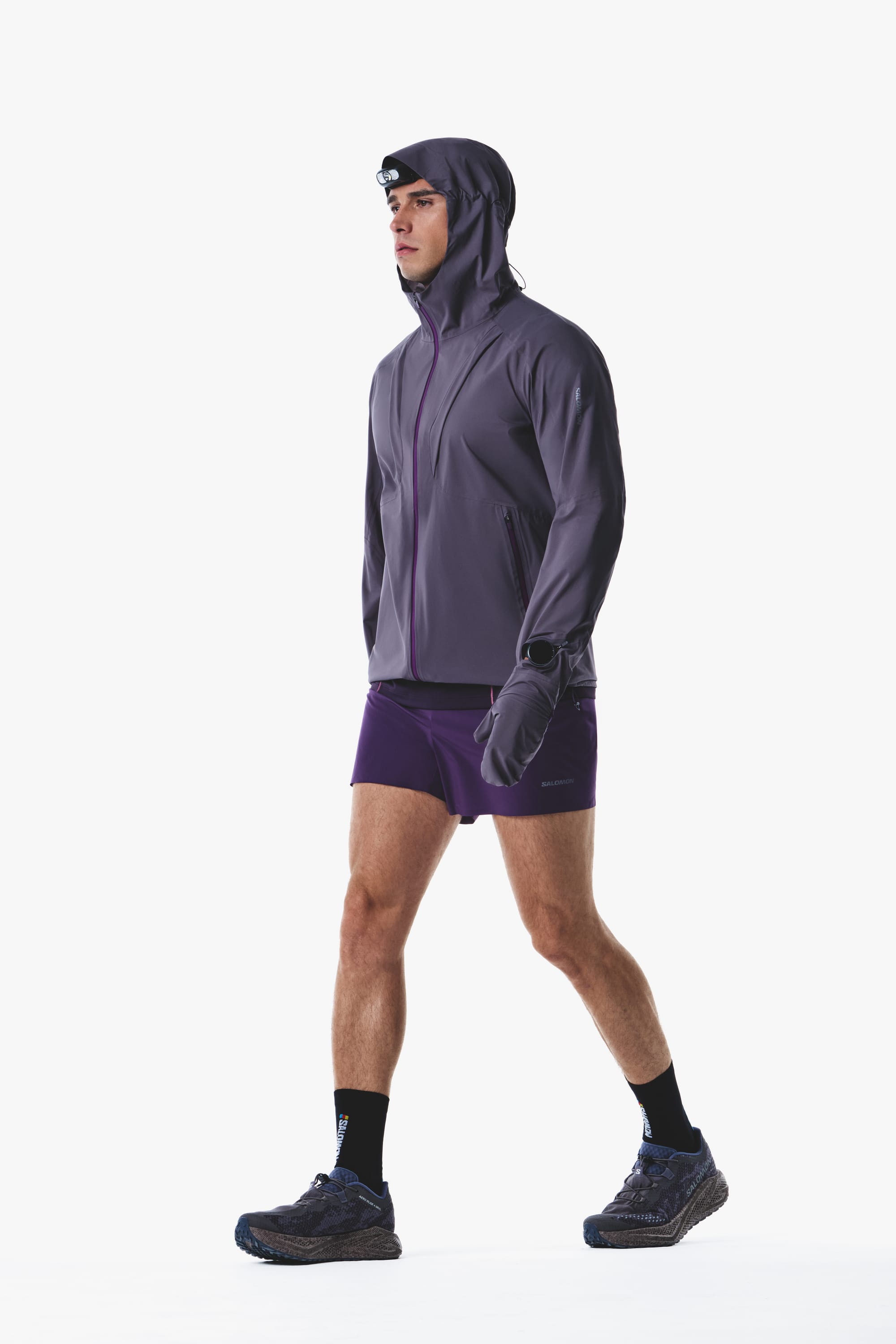 Salomon men's Autumn/Winter 2026 purple hooded trail-running jacket and shorts, walking side view.