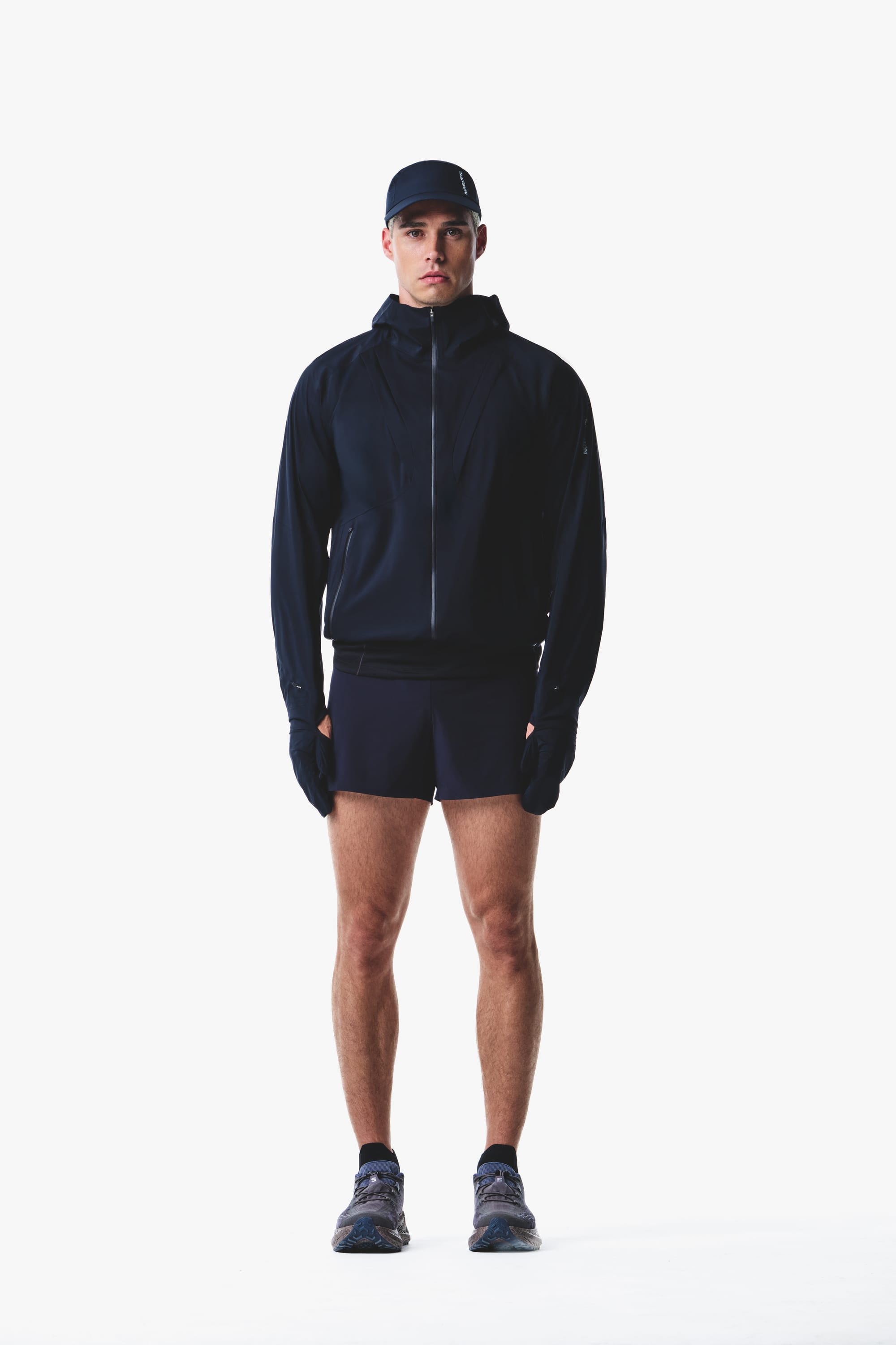 Salomon men's Autumn/Winter 2026 dark navy hooded trail-running jacket and shorts, front view.