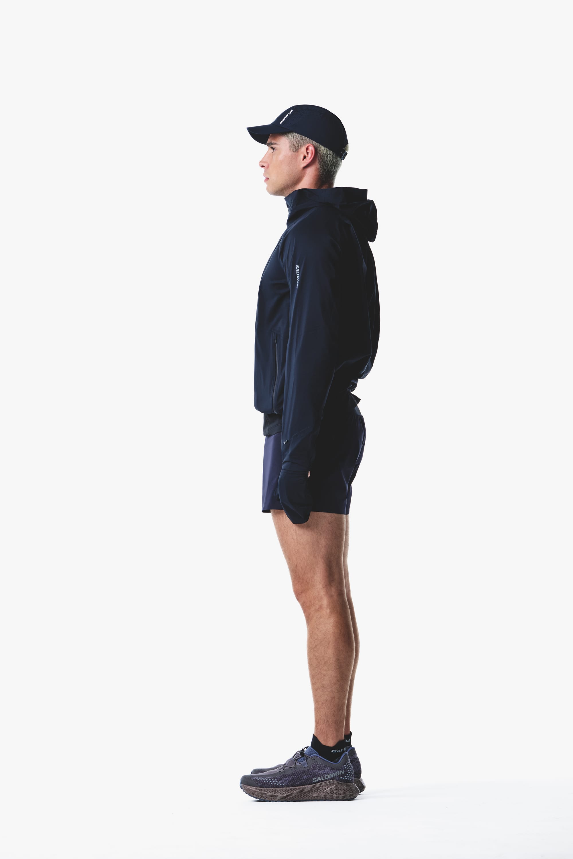Salomon men's Autumn/Winter 2026 dark navy hooded trail-running jacket and shorts, side view.