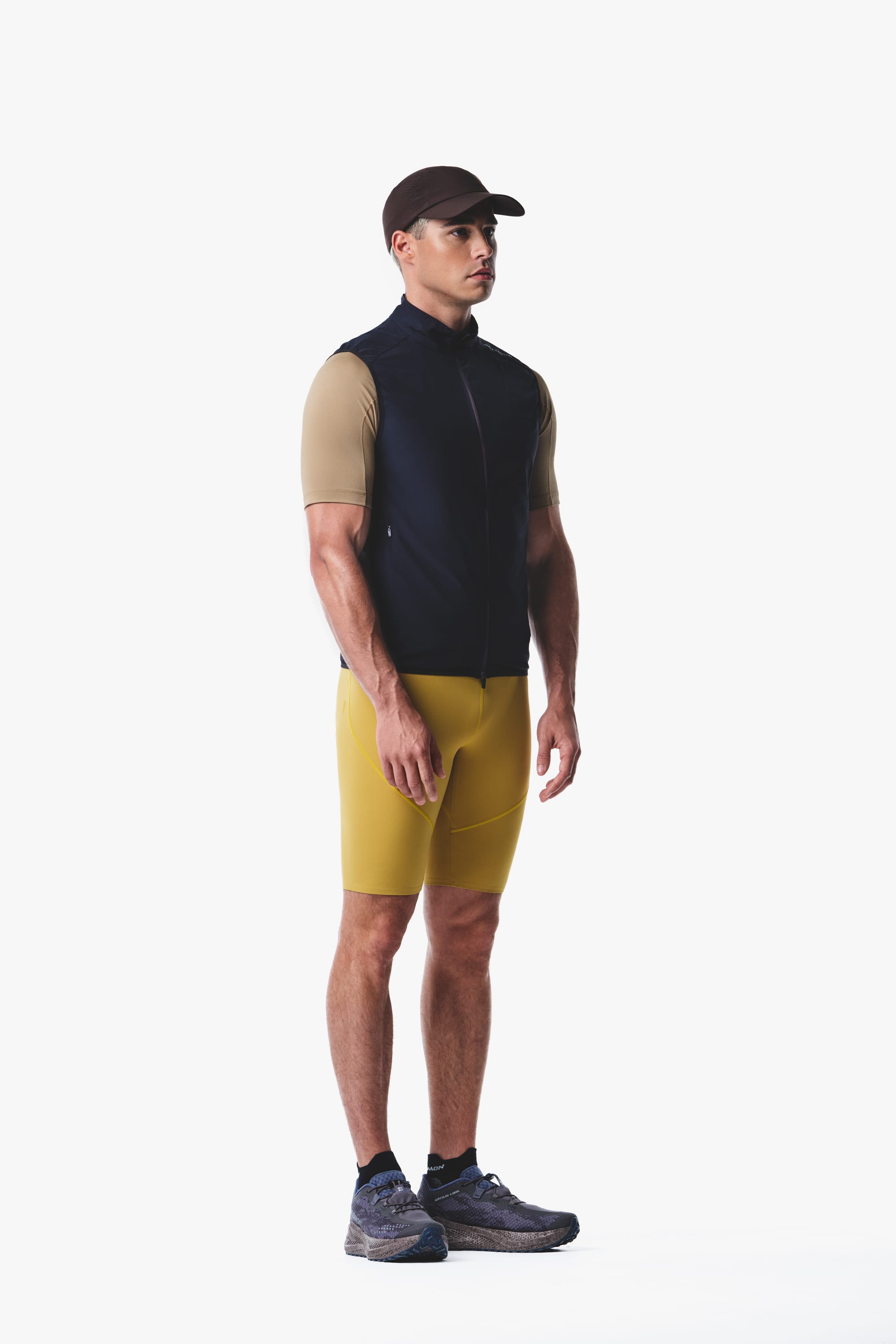 Salomon men's Autumn/Winter 2026 dark sleeveless running vest with yellow fitted shorts, side view.