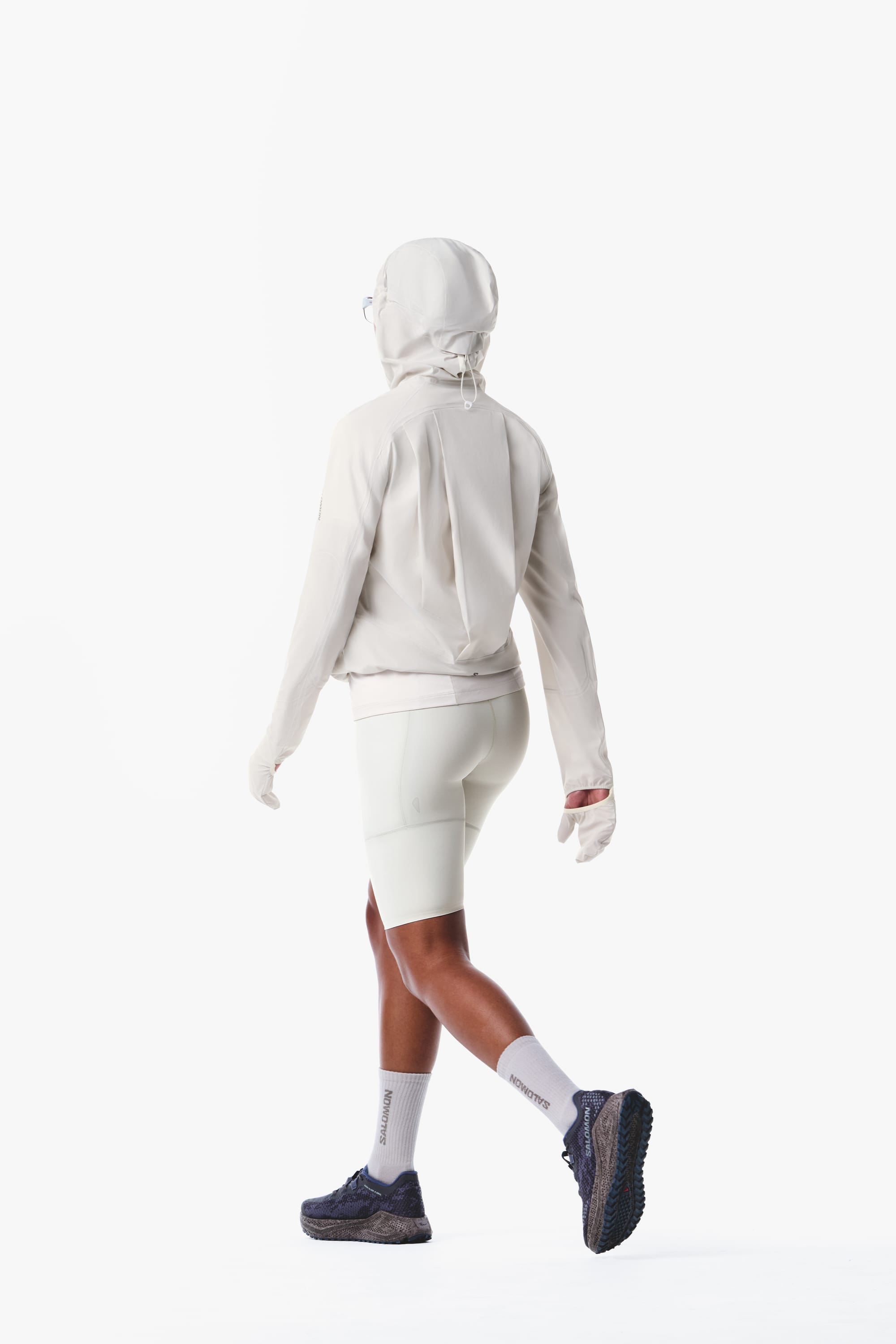 Salomon women's Autumn/Winter 2026 white hooded trail-running jacket and fitted shorts, rear walking view.