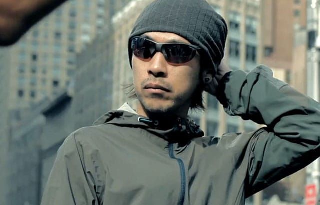 Portrait of a person wearing sunglasses and a hooded technical jacket.