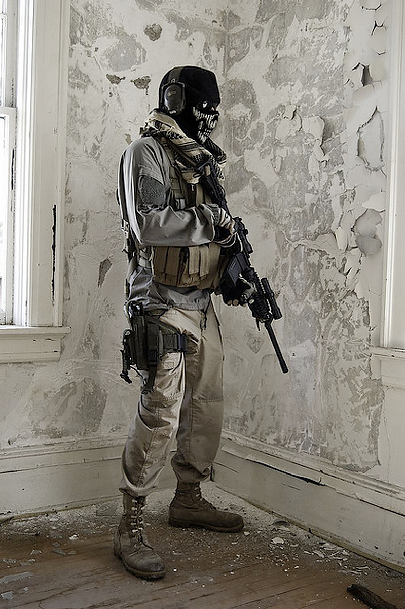 Masked tactical uniform and load-bearing gear in a distressed interior.