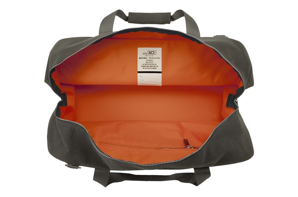 Filson x Ace Hotel tin cloth duffle bag open flat, showing orange interior lining and FILSON [ACE] collaboration label.