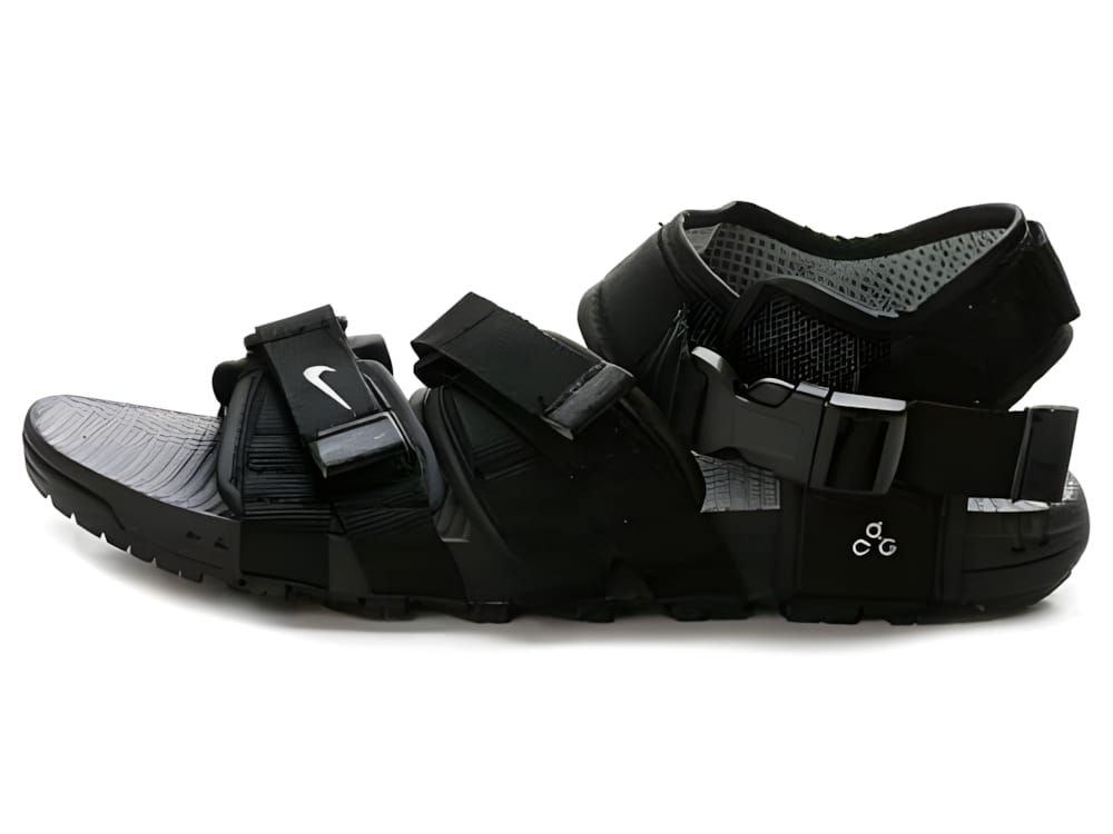 Nike ACG Air Deschutz sandal, lateral view — black nylon straps, white Swoosh, grey footbed, black outsole.