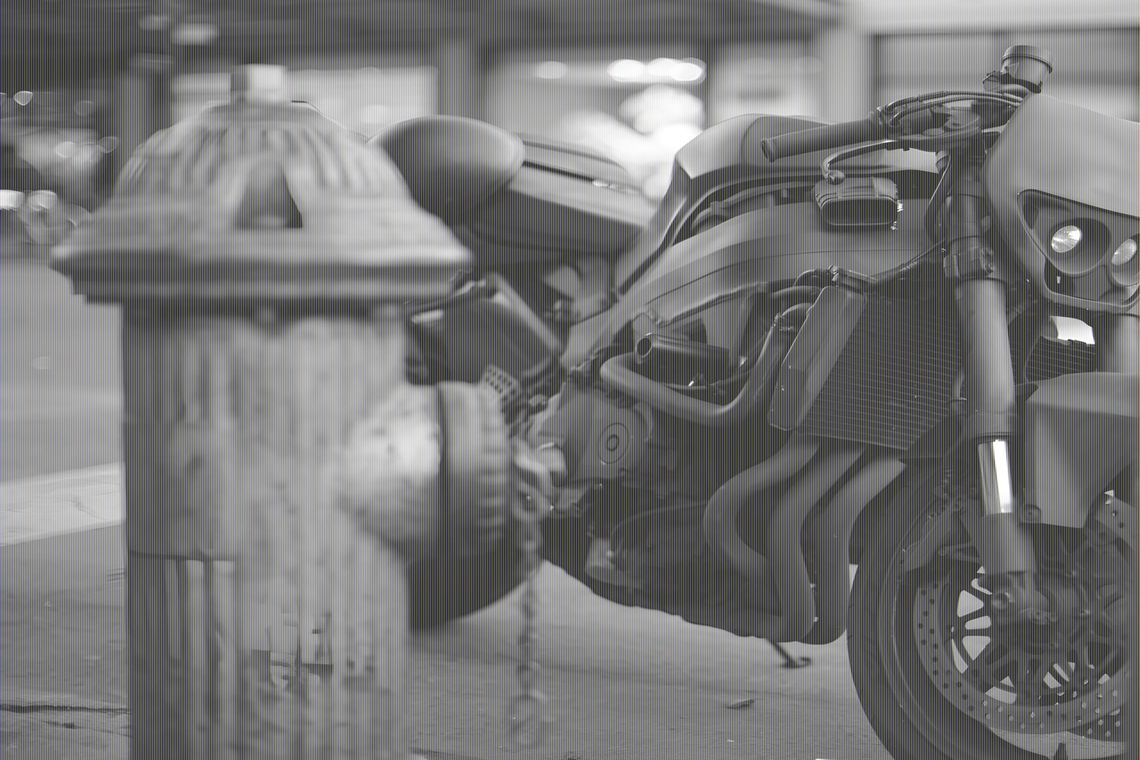 Matte-black Ducati Diavel parked on a city street beside a fire hydrant, trellis frame and V-twin exposed.