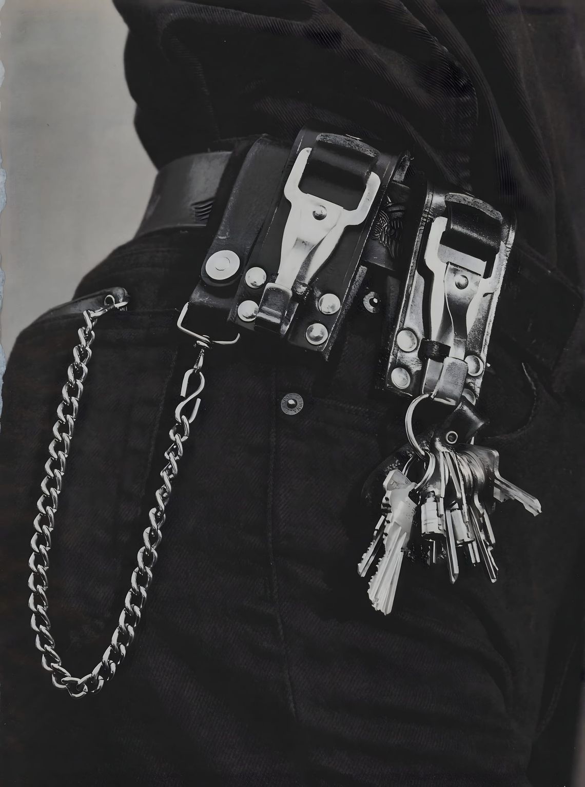 Black-and-white close-up of a waist wearing dark Calvin Klein denim jeans with a wide leather belt, two snap-closure leather 
