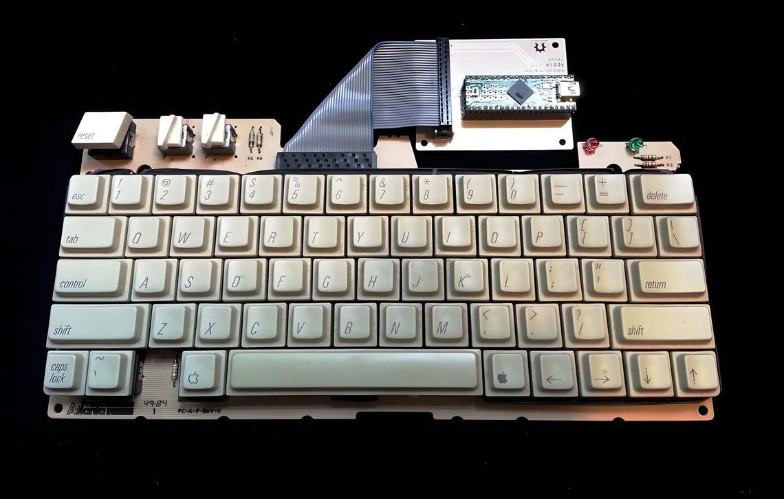 Apple IIgs keyboard PCB with cream Alps keycaps and Arduino Pro Micro USB converter wired via ribbon cable, on black background.