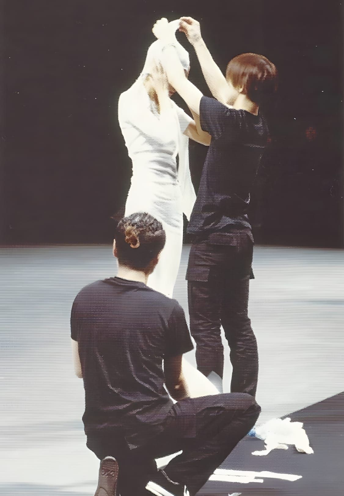 Two dressers in black pull a white seamless tube-knit column garment over a model on the Issey Miyake SS1999 runway.