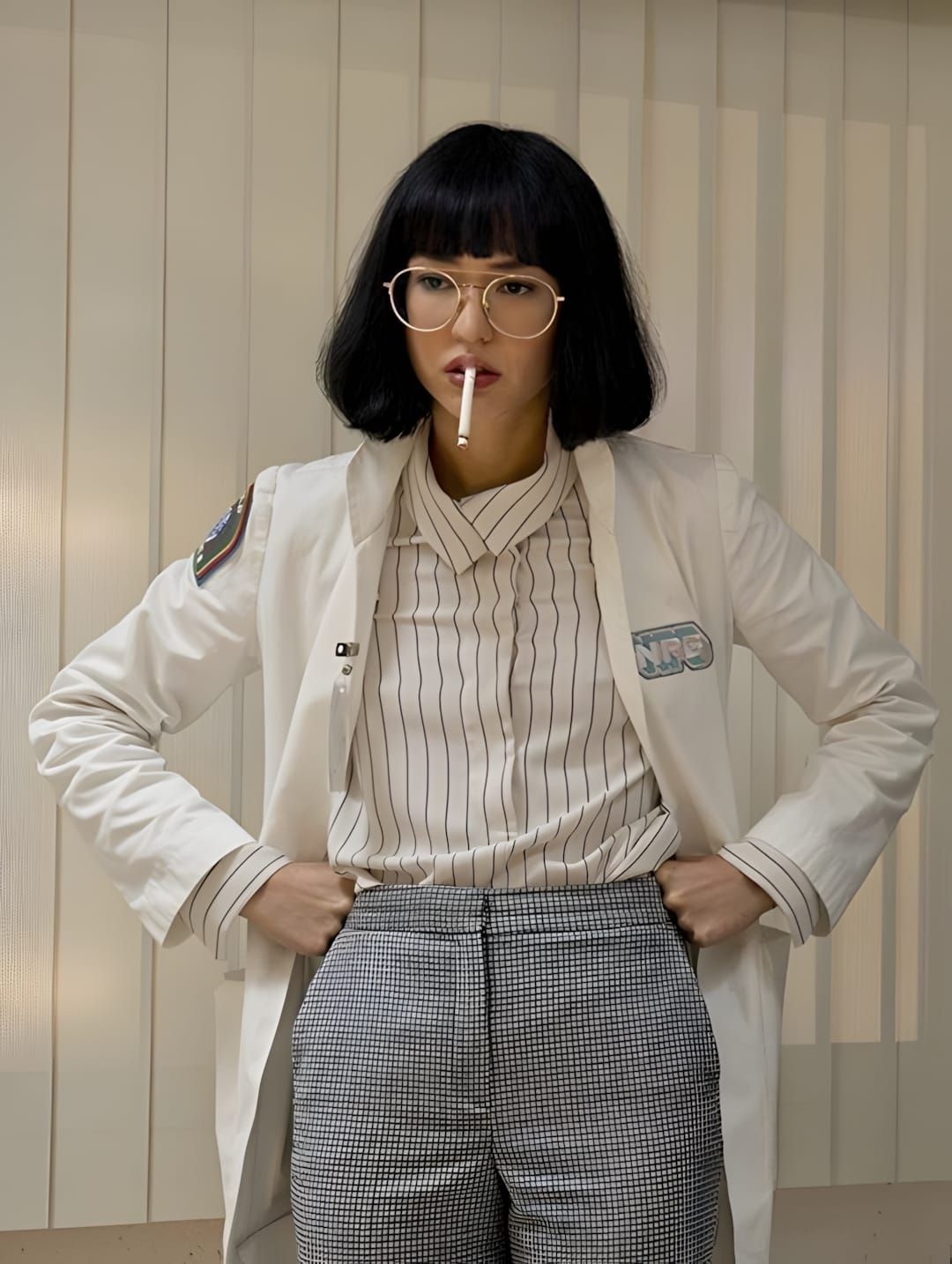 Sonoya Mizuno as Dr. Azumi Fujita in Netflix's MANIAC: white lab coat with NPB chest patch worn open over a black pinstripe c