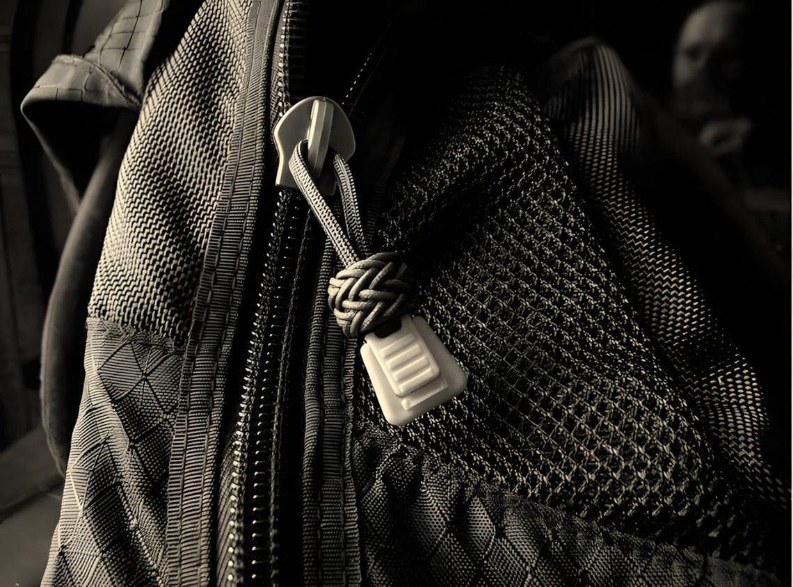 Paracord gaucho knot zipper pull on the zipper of a dark technical backpack, close-up detail.