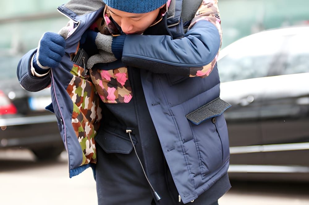 Man in a navy quilted down puffer jacket with a camouflage-print chest accent panel, blue leather gloves, and a blue knit bea