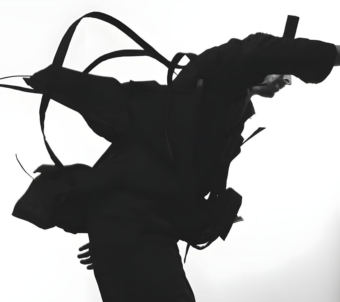 Black-on-white silhouette of figure in motion wearing ACRONYM SS2017 black jacket and chest harness with straps airborne.