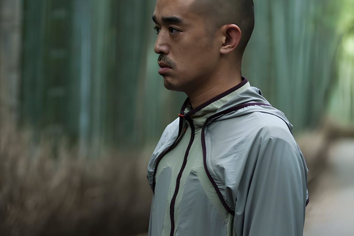 Man in profile wearing a sage green Nike × Undercover Gyakusou FW2011 lightweight hooded running jacket with a chest bib pane