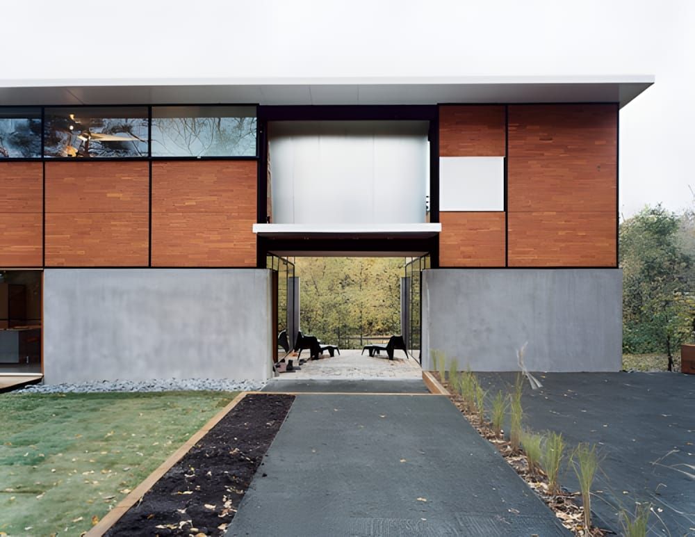Front facade of the FlatPak House: two-storey rectilinear volume with warm cedar-panel upper level, poured-concrete lower bas
