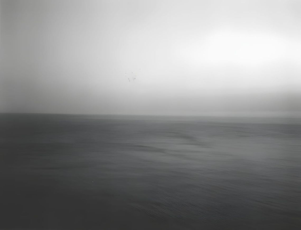 Monochrome large-format photograph bisected precisely at the horizon: calm, dark, textured water filling the lower half; pale