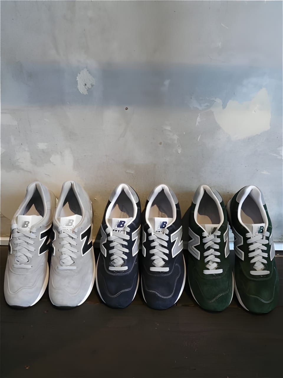 Three pairs of J.Crew x New Balance 1400 Made in USA sneakers lined up on a wooden shelf against a concrete wall — grey (left