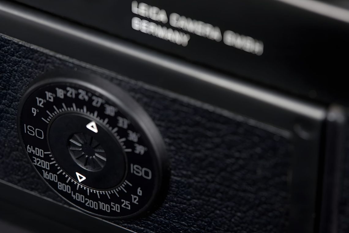 Close-up macro shot of a black Leica M6 rangefinder top plate, showing the circular ISO and shutter-speed dial with markings 