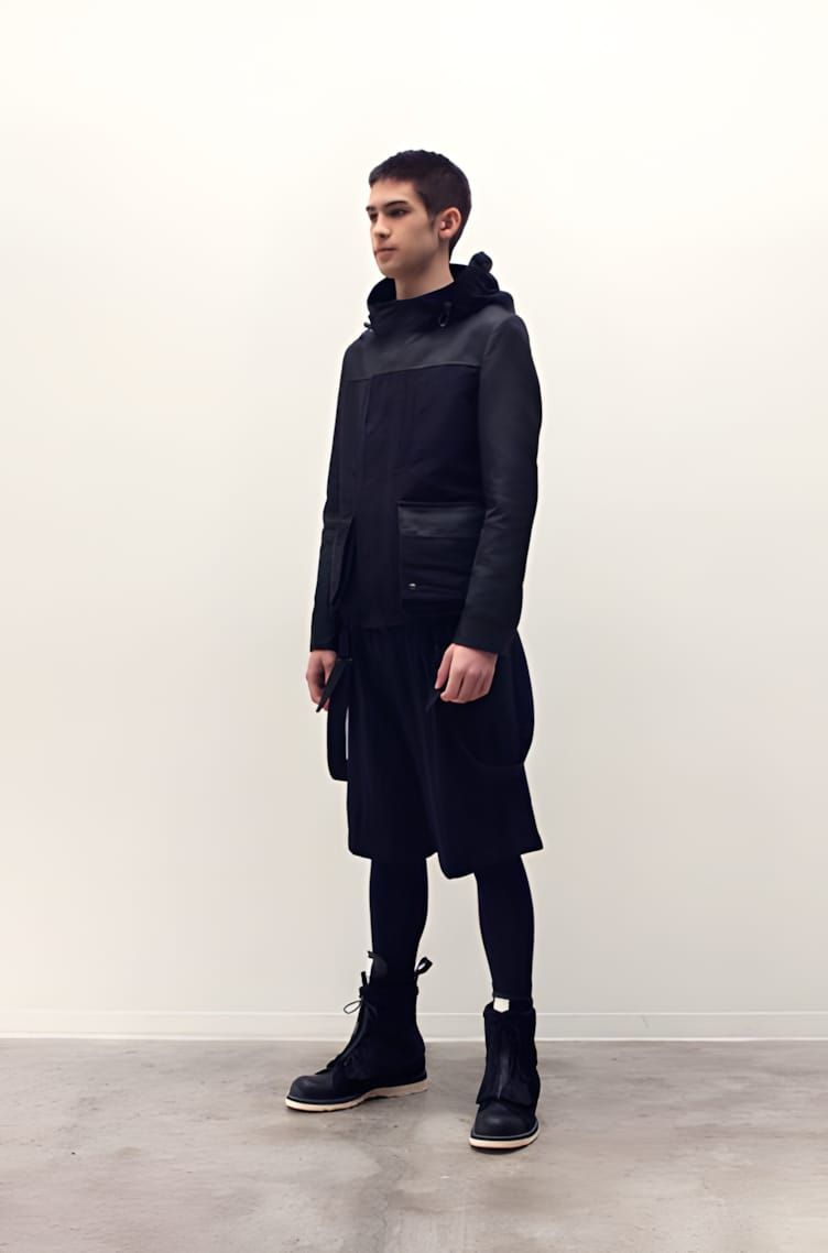 Male model on a white runway floor wearing an all-black Rick Owens FW2009 look: layered structured hooded jacket over a dark 
