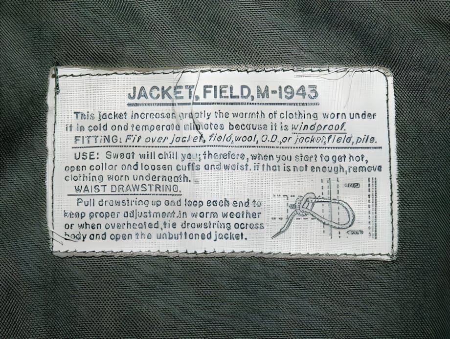 Close-up of the interior cotton spec label from a WWII US Army M-1943 Field Jacket, reading 'JACKET, FIELD, M-1943' with prin