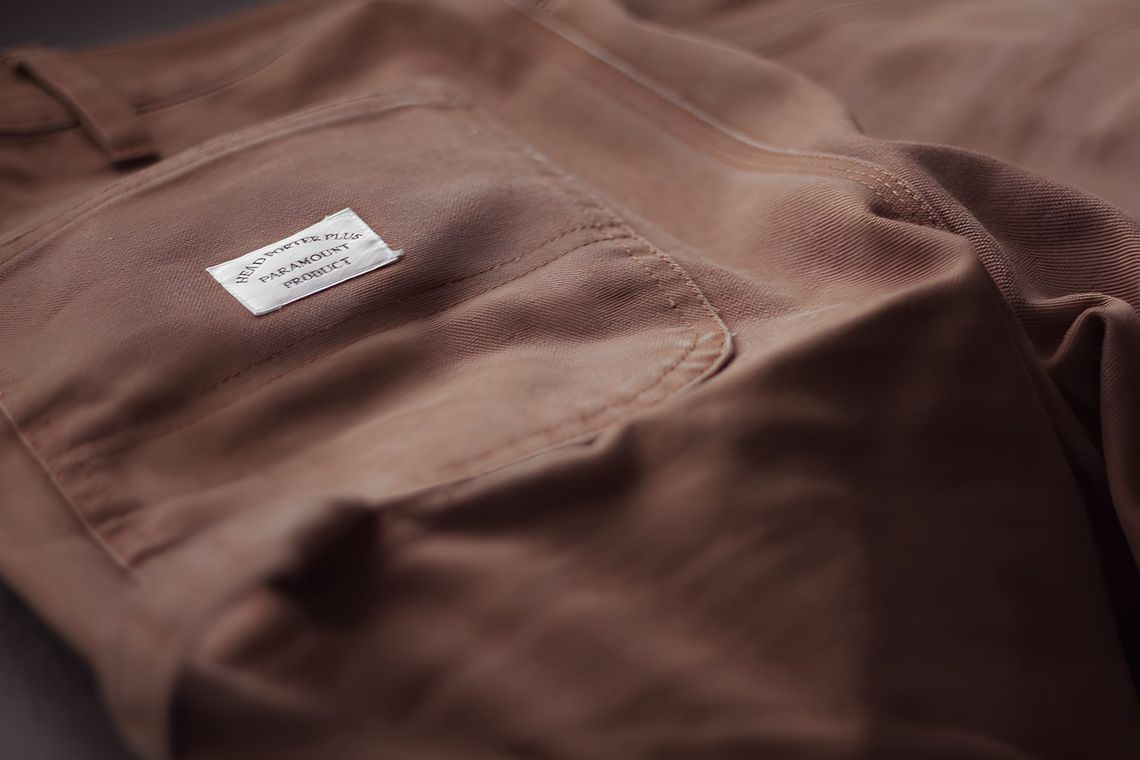 Close-up of a brown heavy cotton twill garment from Head Porter Plus, with a woven label reading 'HEAD PORTER PLUS / PARAMOUN