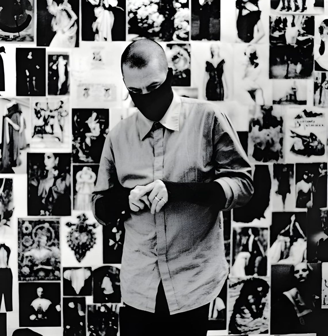 Black-and-white portrait of Alexander McQueen standing in a grey button-front shirt, face obscured by a dark fabric mask, aga