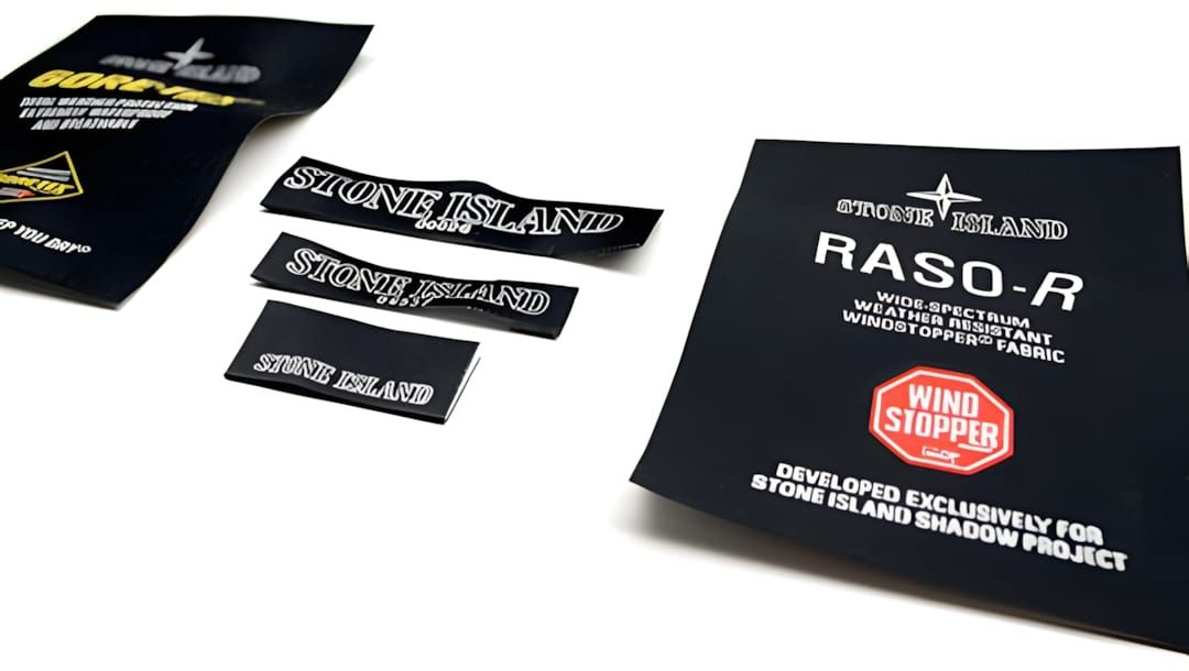 Flat lay of black woven Stone Island Shadow Project garment labels: multiple sizes of the Stone Island wordmark labels and a 