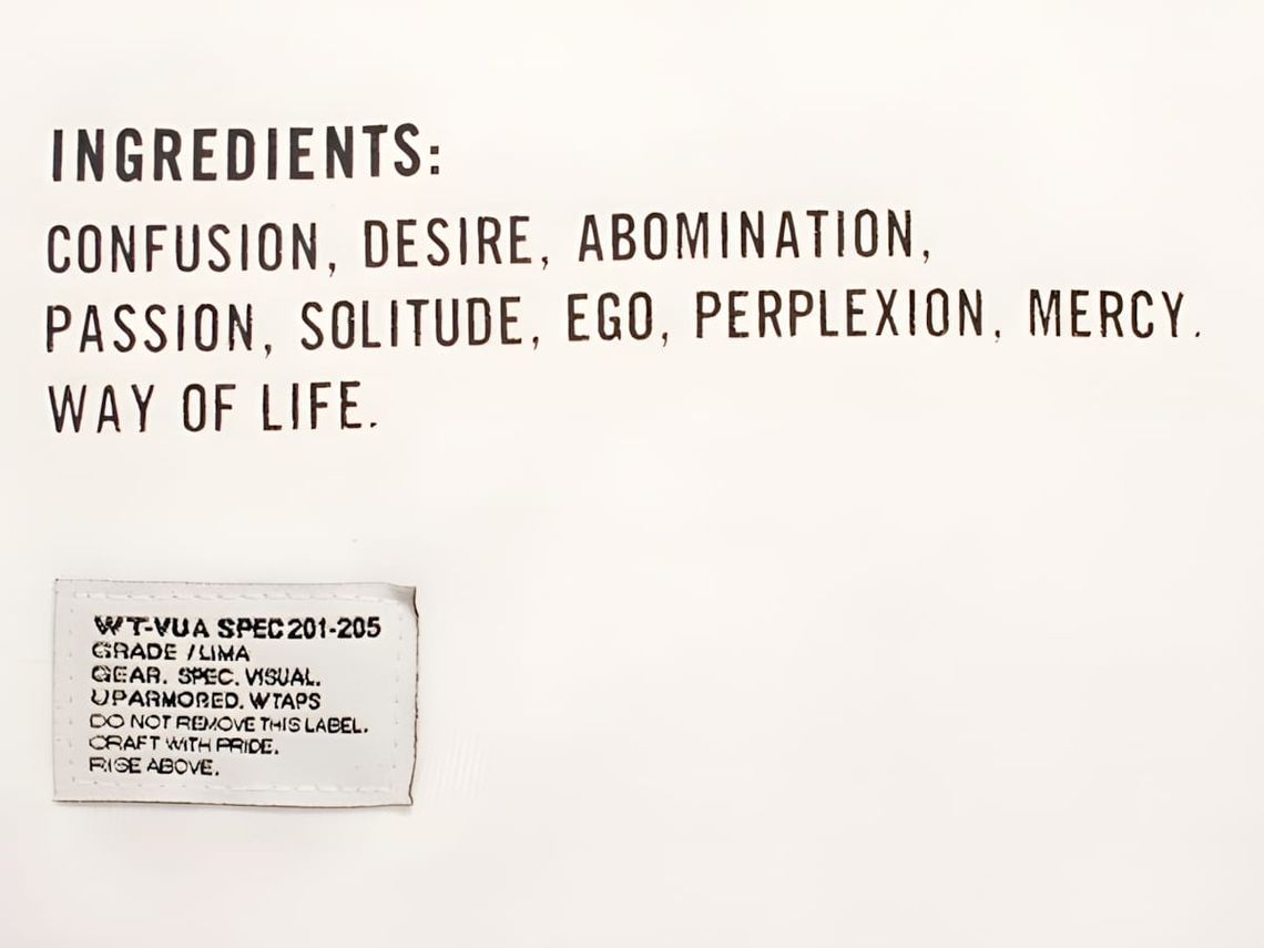 WTAPS garment detail on white fabric: bold screen-printed text reads 'INGREDIENTS: CONFUSION, DESIRE, ABOMINATION, PASSION, S