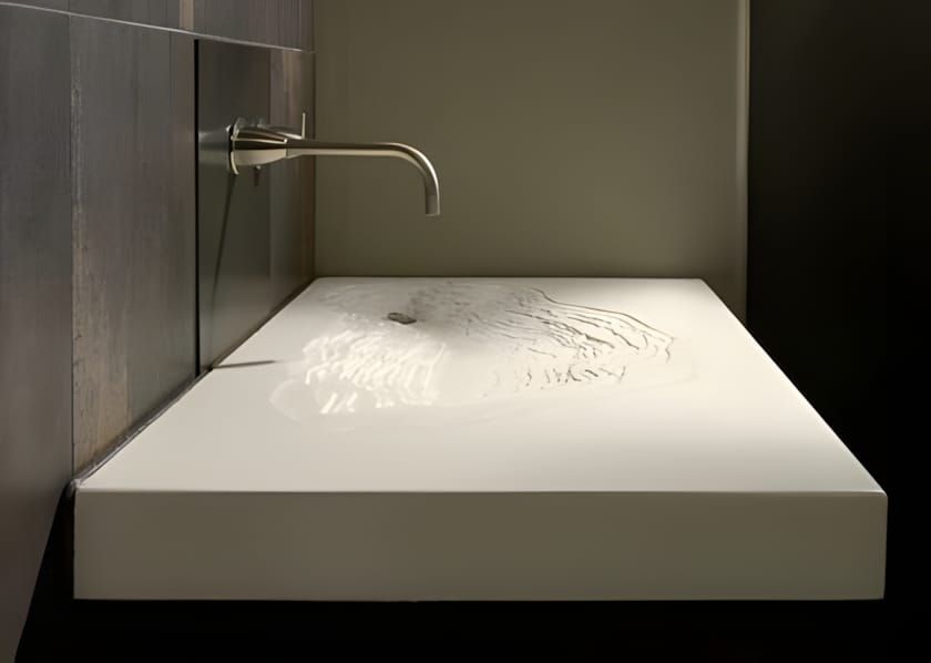 White concrete flat-trough sink with finely etched topographic contour lines on the surface, recessed in a dark stone niche w