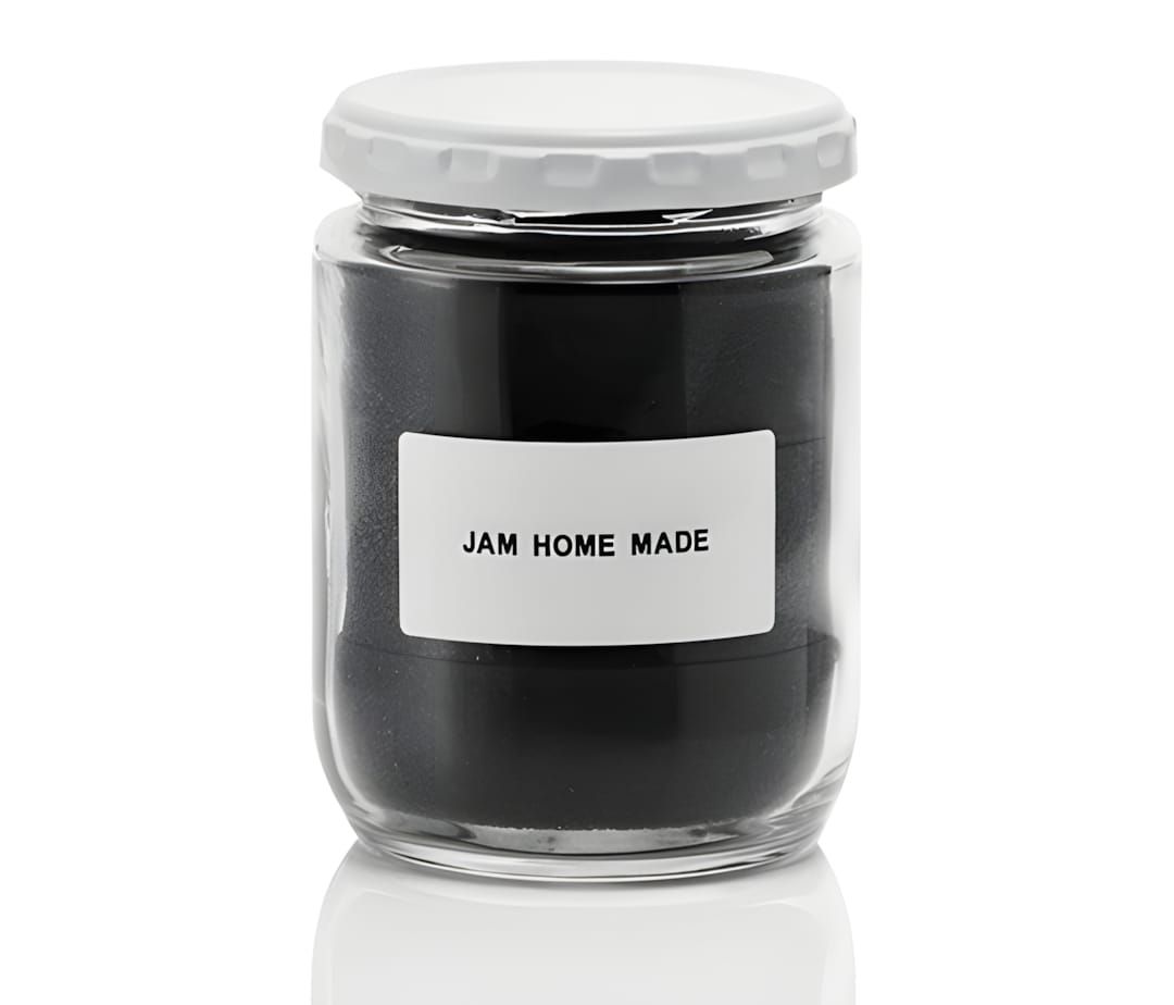 Glass jar filled with dark matte contents, white metal lid, white label reading JAM HOME MADE, on white background.