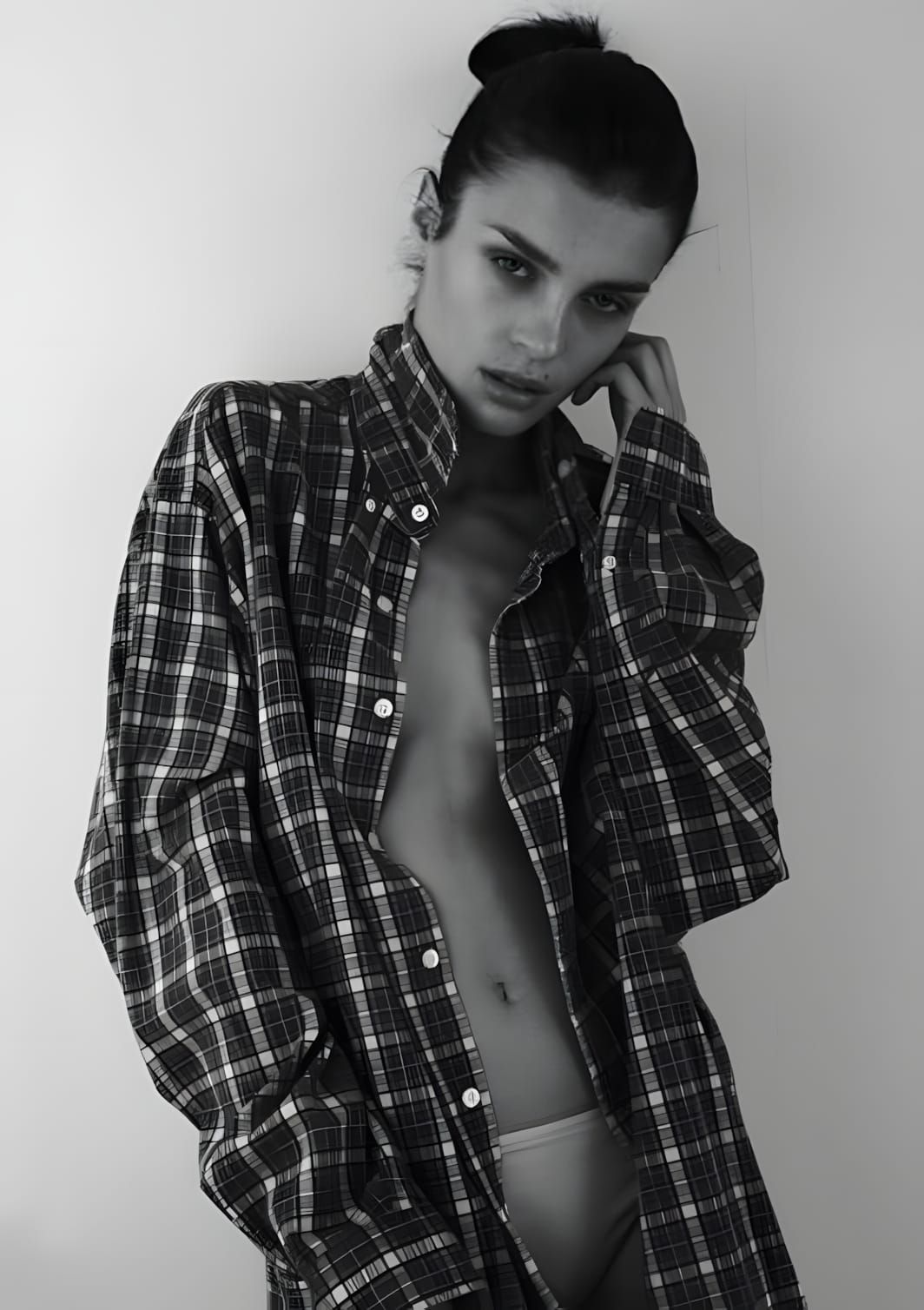 Black-and-white studio portrait of model Olga Boiko wearing an oversized plaid flannel button-up shirt, worn open, hair in a 