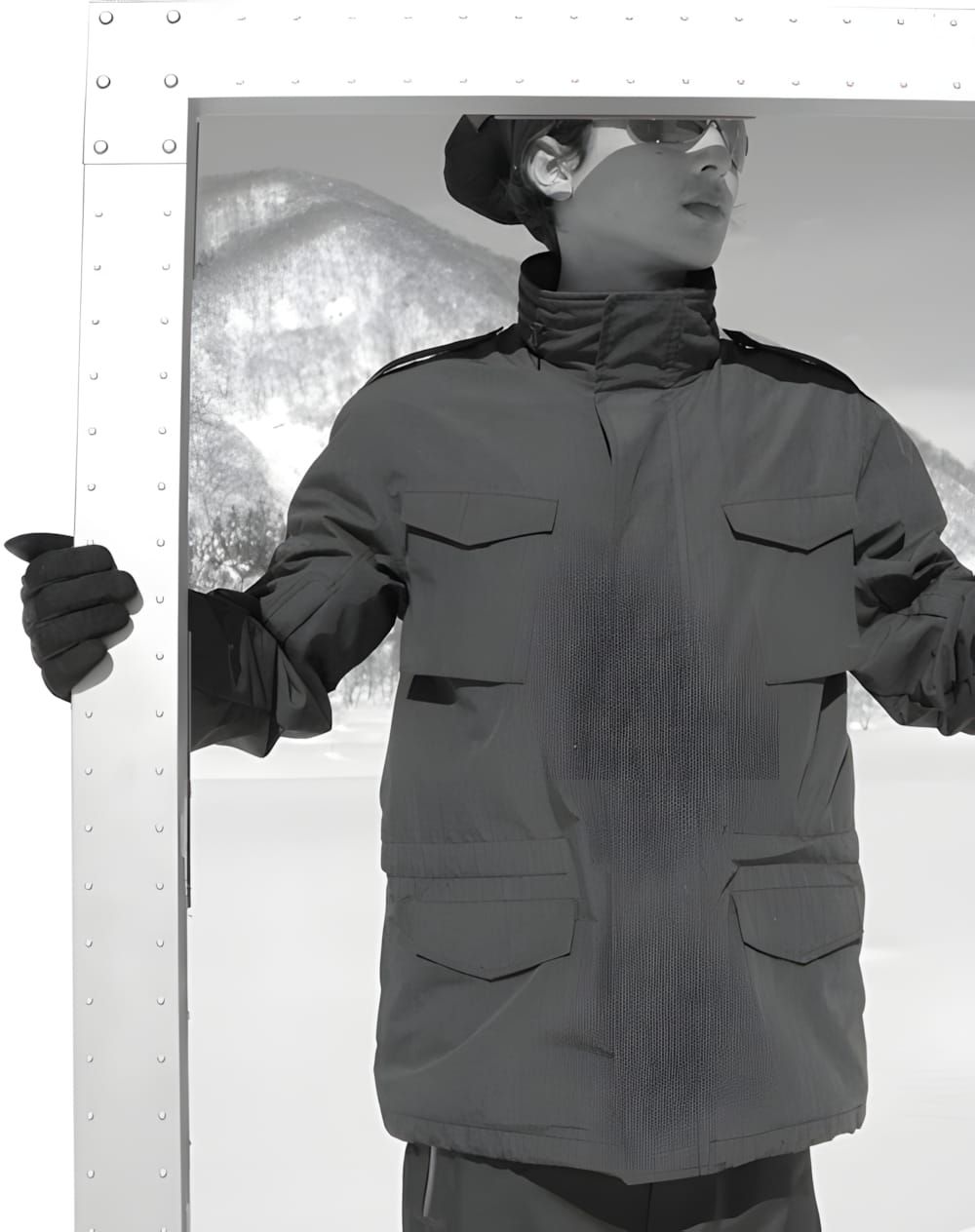 Model in Oakley M65 Tech Jacket, four flap pockets, stand collar, tactical gloves, snowy mountain backdrop.