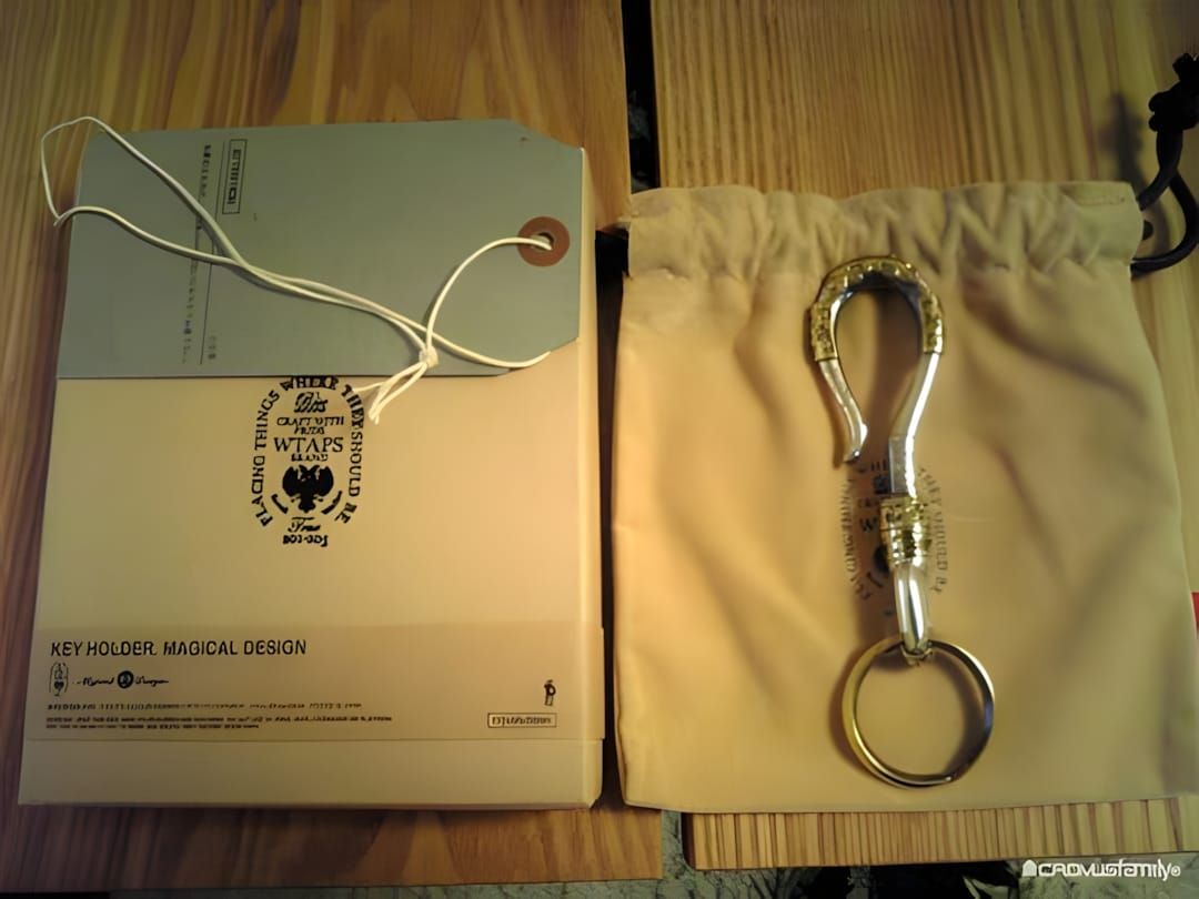 WTAPS 'Key Holder, Magical Design' — a gold-tone brass carabiner-style key holder with engraved detailing and split key ring,