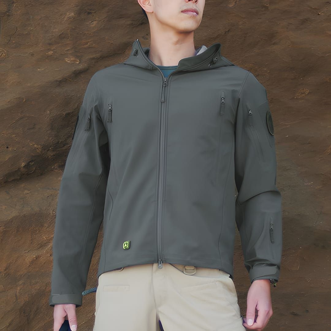 Man wearing TAD Gear Stealth Hoodie in foliage grey-green softshell with diagonal chest zips and green rubber TAD logo patch,