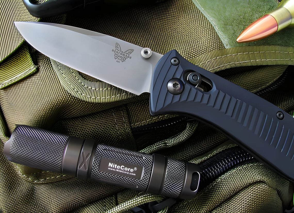 Benchmade Griptilian 550 open, blue handle, satin drop-point blade, with tactical flashlight and cartridge on green surface.