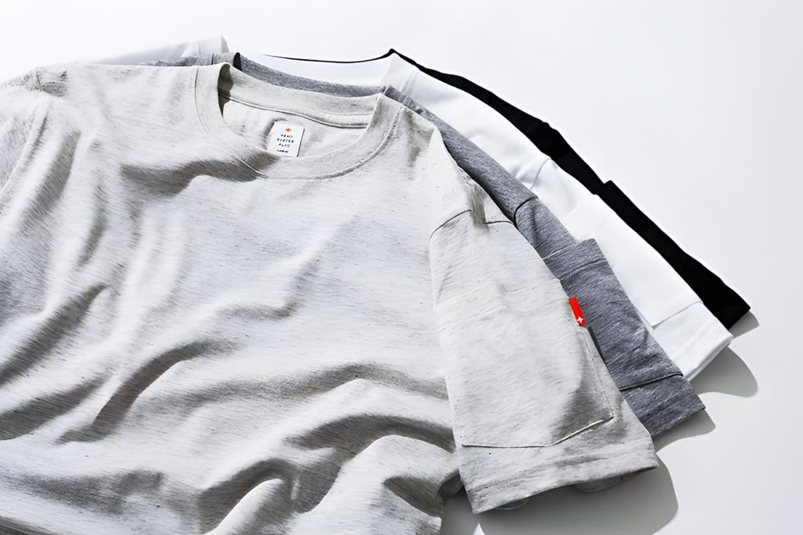 Four Champion Reverse Weave Classic Crew Neck tees stacked in grey marl, white, mid-grey, and black colorways.