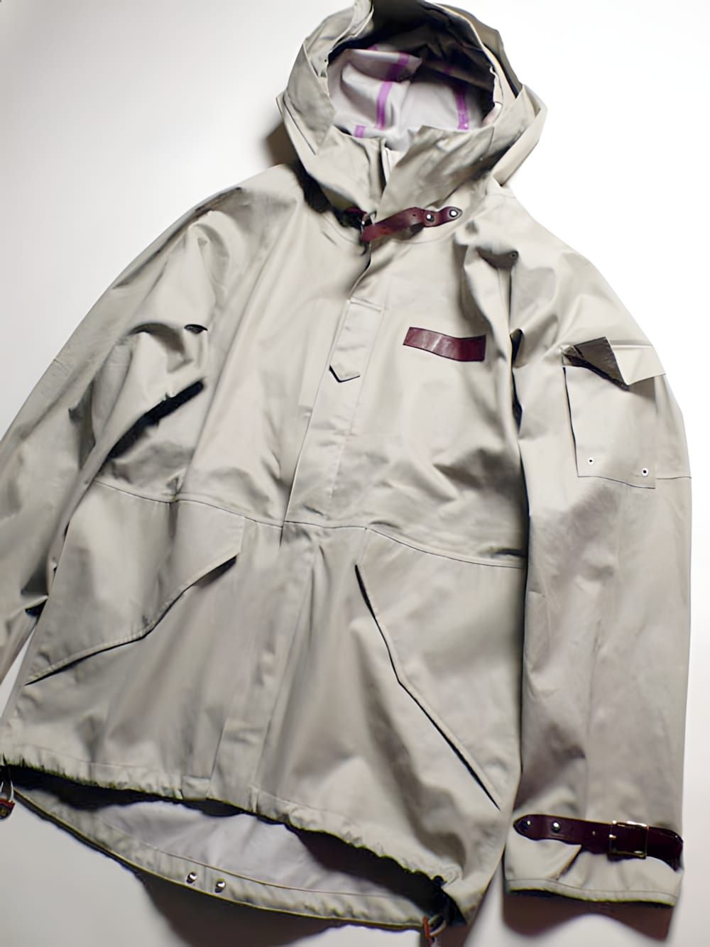 Visvim Nomad jacket in stone/khaki — smock-style technical shell with hooded plaid lining and riveted burgundy leather strap 