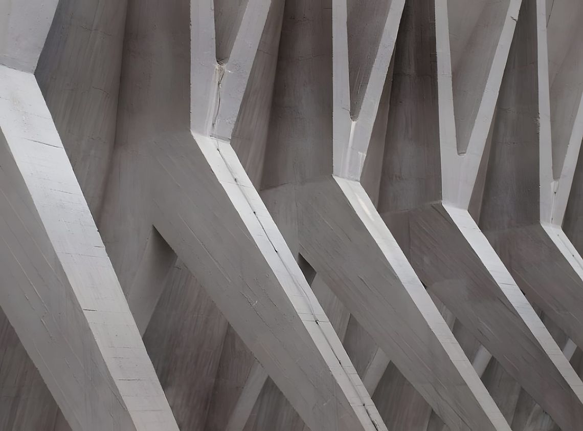 Close-up of angular intersecting white-painted reinforced concrete structural ribs forming a zigzag geometric pattern — inter