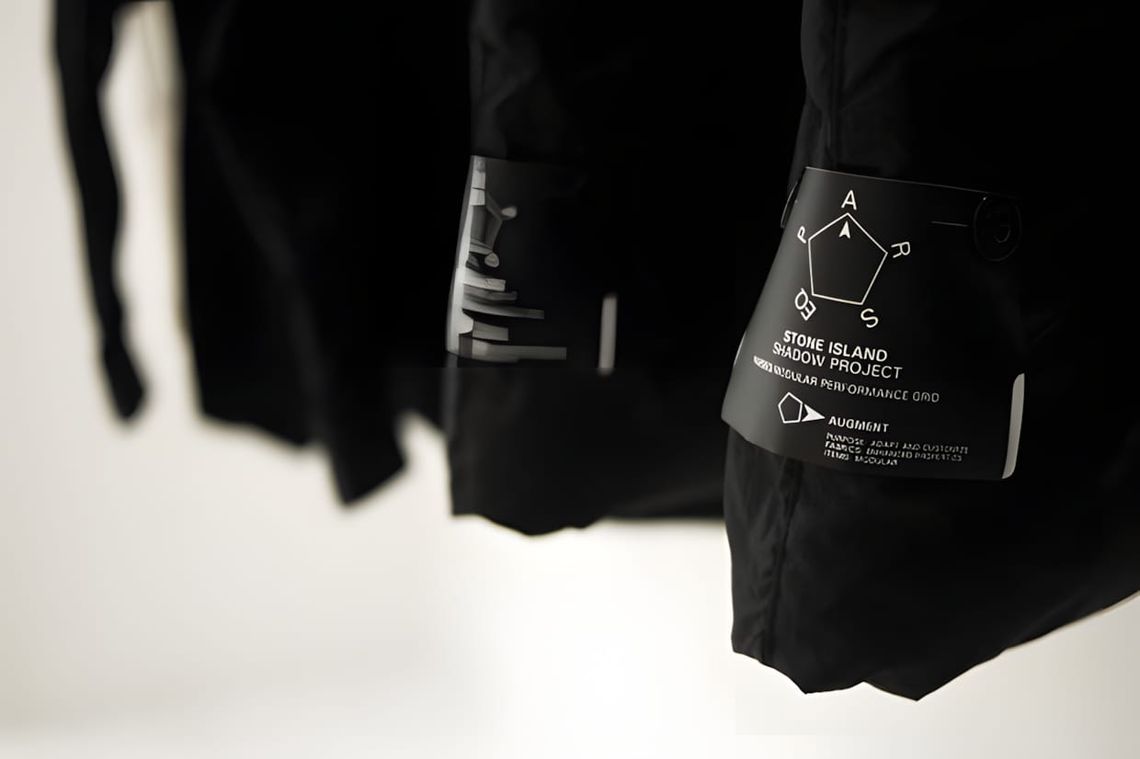 Close-up of a Stone Island Shadow Project PARSEQ Modular Performance Grid label tag on black outerwear, showing the AUGMENT c