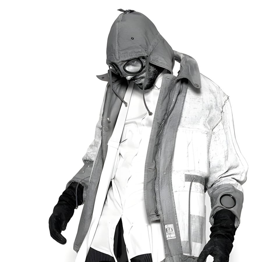 Figure in C.P. Company × Aitor Throup 1000 Miles Goggle Jacket, round goggle lenses raised over face, structured hood, Tinto 