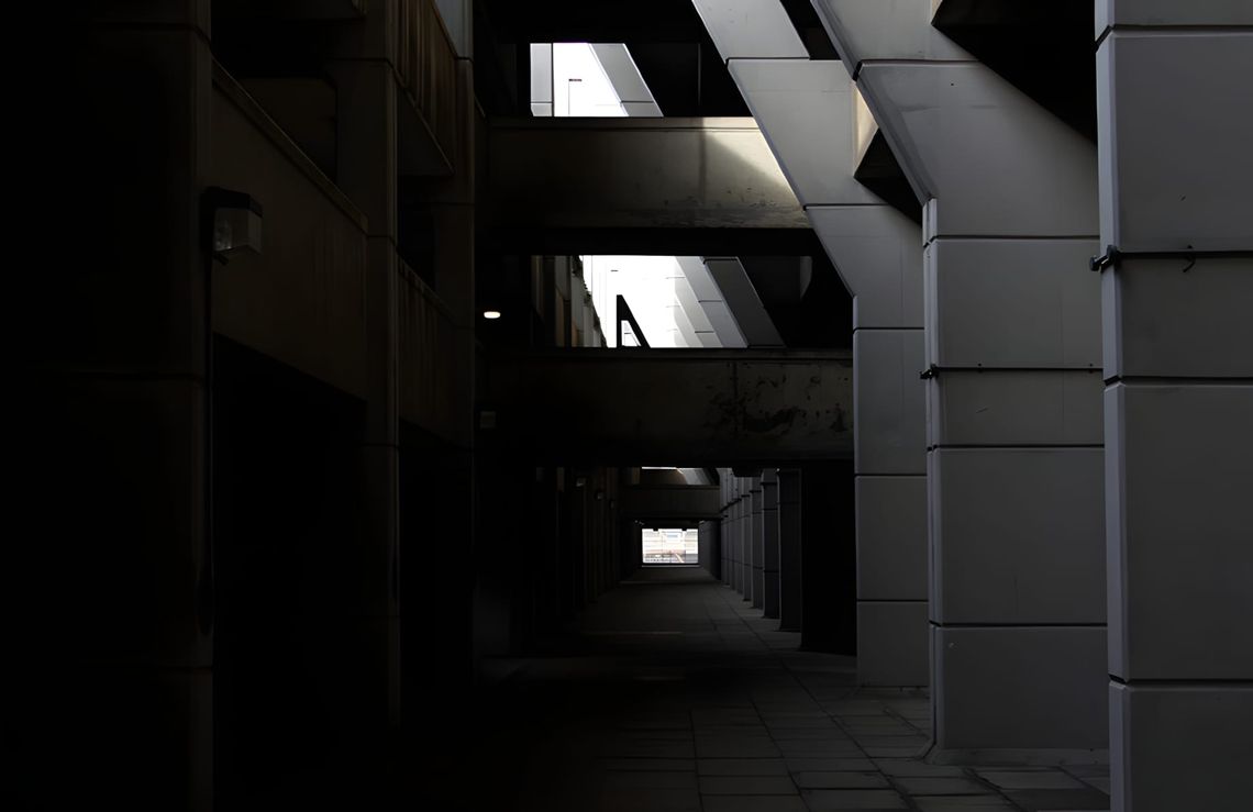 Dark undercroft walkway beneath Preston Bus Station, angled concrete soffits overhead, panelled columns right, tunnel recedin
