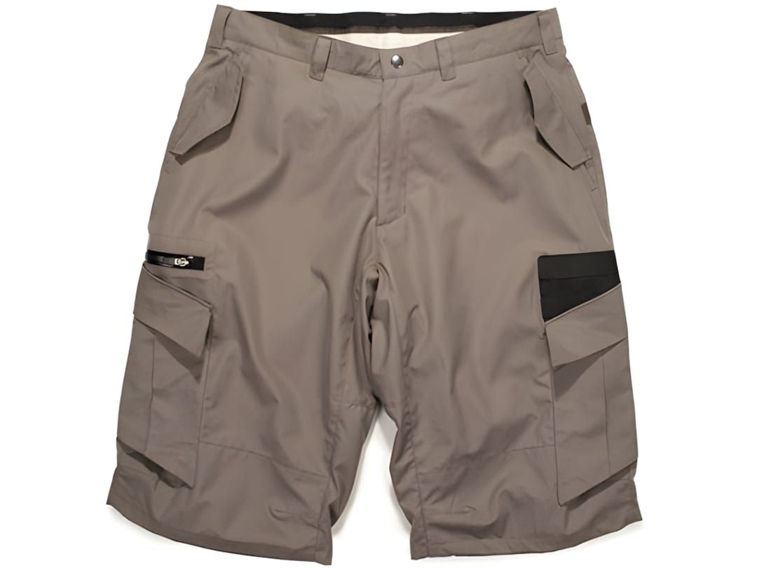 ZOIC Ether men's mountain bike shorts in tan ripstop, ghost-mannequin flat-lay, diagonal black contrast panel on right thigh 