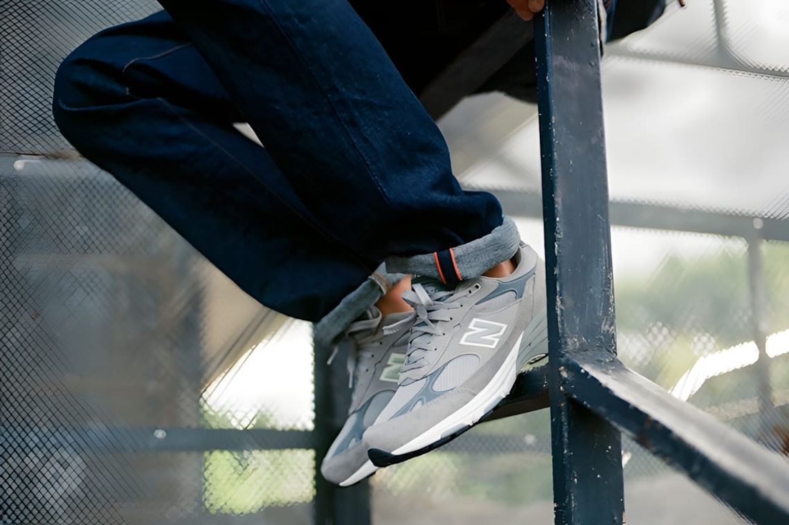 New Balance 993 in grey suede and mesh worn on feet on a steel fire escape, side profile, indigo denim jeans